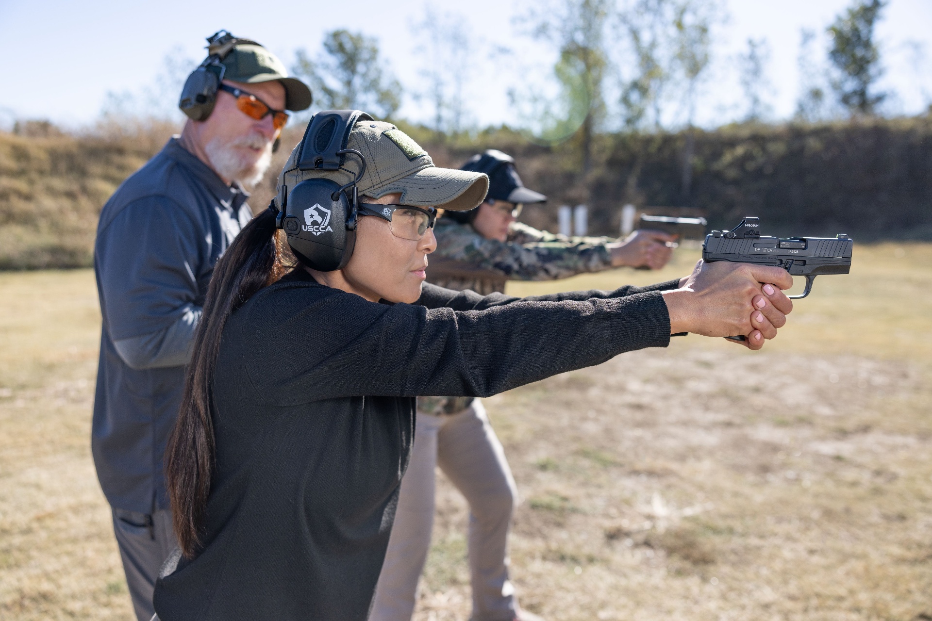 Trainee practicing handgun fundamentals at an indoor range with eye and ear protection